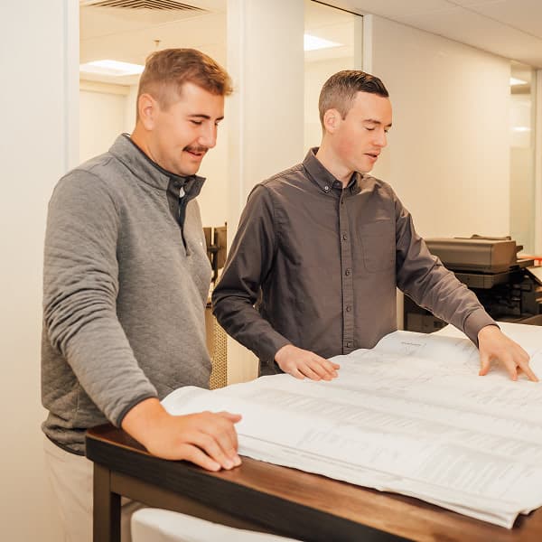 Two colleagues review large blueprints spread across a table