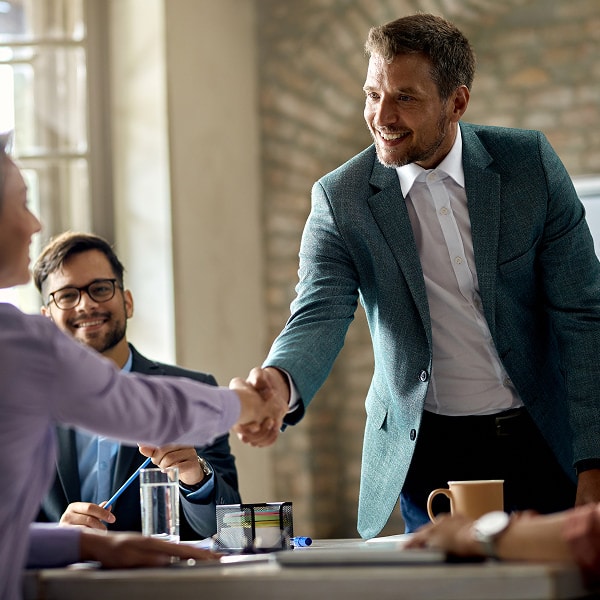Two colleagues shake hands across a conference table during a business meeting